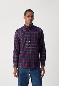 Camisa de cuadros en navy, burdeos y blanco; de manga larga; con cuello; material de algodón; botones visibles; corte casual; combinada con jeans de denim azul.