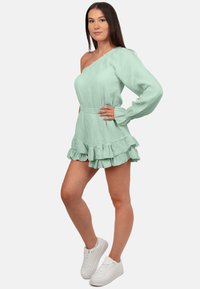 Mintgroene één-schouderjurk met lange mouwen, textuurstof, gerimpelde zoom en gecombineerd met witte sneakers.