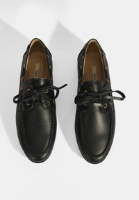 Schwarze Lederschuhe mit runder Zehenform, Schnürung vorne mit goldenen Ösen und strukturiertem Nähen entlang der Kanten.