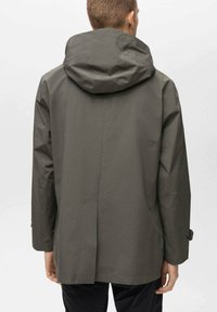 Jachetă impermeabilă verde închis, cu glugă, având un croi drept și un design minimalist. Țesătura pare netedă, fără modele vizibile.