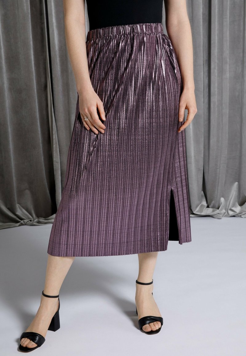 Jupe midi plissée en violet métallisé avec une taille élastique et une fente sur le côté, assortie avec des sandales à talons noires. Texture lisse et brillante.