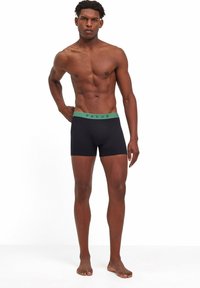 Schwarze Boxershorts mit einem grünen elastischen Bund. Gefertigt aus glattem Stoff, mit einer engen Passform und einem schlichten Design. Keine Muster oder Akzente.