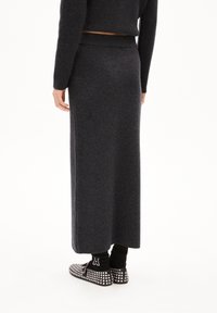Długa, ciemnoszara dzianinowa spódnica z dopasowanym pasem, zestawiona z czarnymi butami z ćwiekami. Materiał wydaje się miękki o gładkiej fakturze.