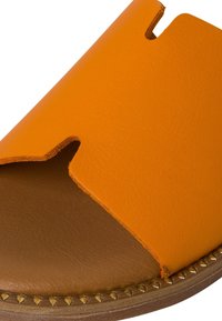 Orange läderslid sandal med öppen tå och utskurna detaljer; har en brun innersula och ett guldnitar accent runt sulan.