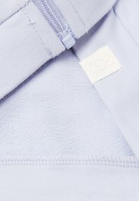 Primo piano di un tessuto blu chiaro con una cerniera e un'etichetta bianca cucita che presenta un piccolo logo di coniglio.
