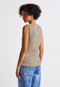 Tajta, ärmlös tank i ljusbeige ribbad tyg, bakvy. Buren med högmidjade, lösa blå jeans i denim med fickdetaljer.