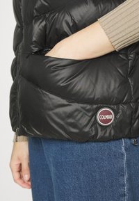 Giacca piumino nera con finitura lucida, dotata di una tasca con zip e di un patch rotondo del logo Colmar sul lato sinistro in basso.