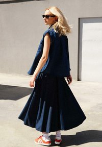 Haut en denim sans manches bleu foncé associé à une jupe fluide bleu foncé, des chaussettes blanches et des baskets rayées orange. Texture lisse ; design décontracté.