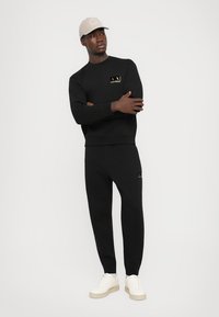 Black sweatshirt and joggers made of soft fabric, featuring a gold logo. Paired with a light beige cap and cream sneakers.
