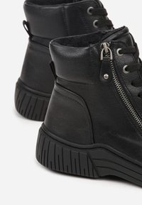 Bottines en cuir noir avec une finition texturée, détail de fermeture éclair en métal, et semelle en caoutchouc épaisse avec un motif nervuré pour une meilleure adhérence.