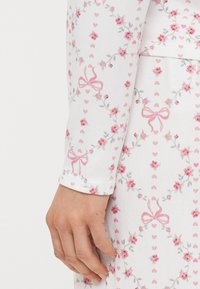 Μπλούζα με μακριά μανίκια από λευκό ύφασμα με σχέδιο λουλουδιών και καρδιές σε ροζ και γκρι, με απαλή υφή και εφαρμοστά μανσέτα.