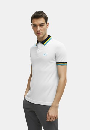 Maglietta polo bianca con colletto blu navy, righe blu e gialle, maniche corte e un piccolo logo blu sul petto.