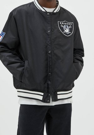 Veste varsity Black Raiders avec boutons-pression, poignets et ourlet à rayures blanches, écusson de marque sur la poitrine et logo NFL sur la manche.