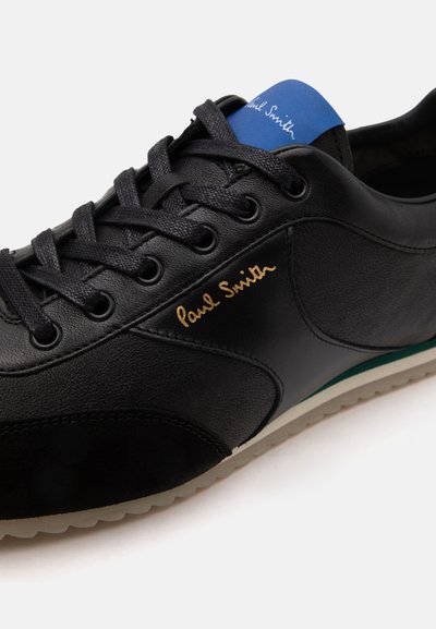 Baskets en cuir noir avec lacets noirs, logo doré "Paul Smith" sur le côté, et languette en tissu bleu affichant le texte blanc "Paul Smith".