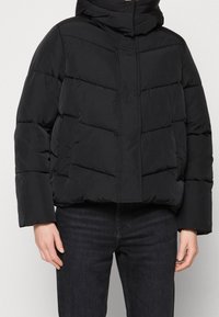 Svart puffjacka med hög krage, oversized passform, kviltat mönster och dragkedja fram. Har breda ärmar och sidofickor.