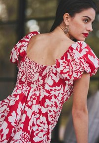 Röd blommig klänning med puffärmar, med en smockad bodice och en bred, öppen ryggdesign. Slätt tyg med en lös passform.