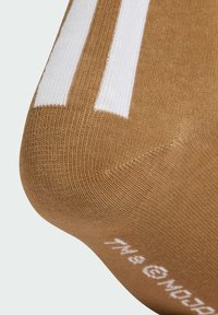 Brązowa skarpeta prążkowana z białymi paskami na mankiecie. Teksturowana dzianina. Okrągły palec i pięta. Dekoracyjny biały tekst na podeszwie.