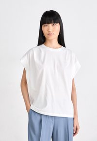 Maglietta in cotone bianco con maniche corte arrotolate. Collo rotondo e vestibilità rilassata, abbinata a pantaloni azzurri chiari. Design semplice e minimale.