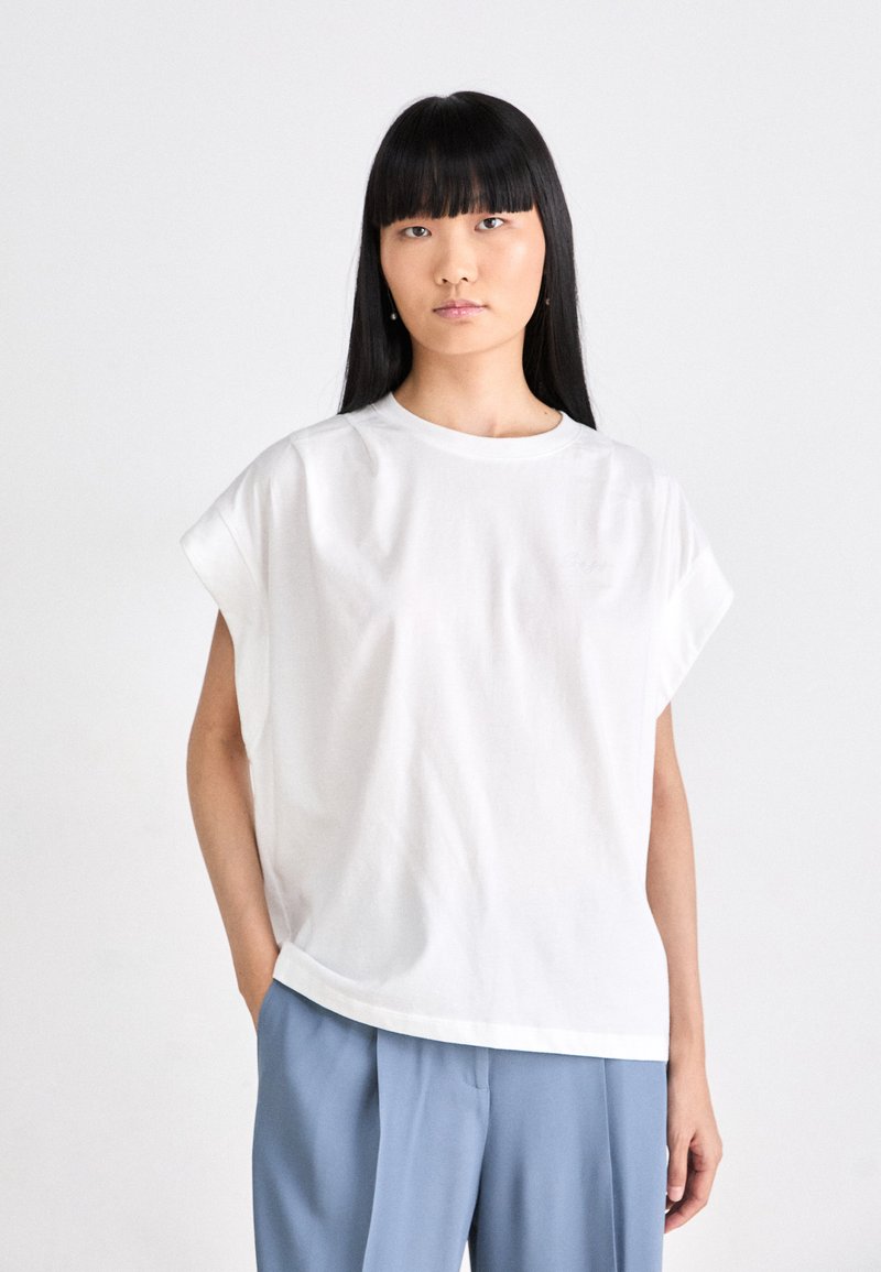Maglietta in cotone bianco con maniche corte arrotolate. Collo rotondo e vestibilità rilassata, abbinata a pantaloni azzurri chiari. Design semplice e minimale.