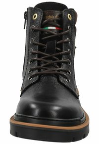 Botín de cuero negro con cordones marrones, ojales dorados y suela de goma. Presenta una cremallera lateral y un acento multicolor en la lengüeta.
