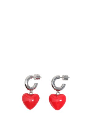 Pendientes de aro plateados con dijes brillantes en forma de corazón rojo colgando de cada aro sobre un fondo blanco.