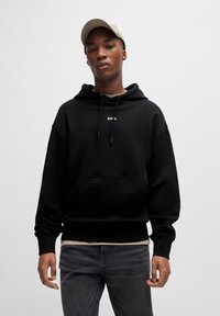 Zwarte hoodie met een voorzak en een trekkoordcapuchon, voorzien van witte tekst "BOSS." Draag hem over een licht shirt en combineer met donkere jeans.