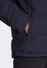 Marinblå puffer-jacka med slät textur, vadderad design och dragkedjefickor för funktionalitet.