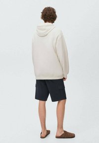 Beige huva sweatshirt, mörka cargoshorts och bruna sandaler. Avslappnad passform, mjukt material och synlig sömnad på sweatshirten.