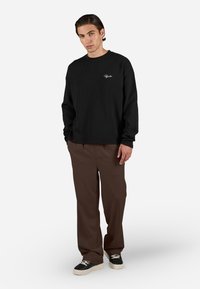 Fekete, texturált pulóver kerek nyakkal, kis logóval. Barna nadrággal és fehér talpú fekete tornacipővel párosítva.