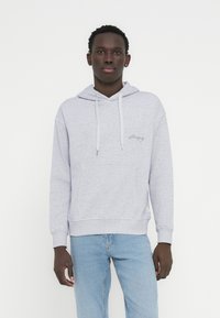 Ανοιχτό γκρι φούτερ με κουκούλα, κατασκευασμένο από απαλό ύφασμα, με μπροστινή τσέπη, ρυθμιζόμενη κουκούλα με κορδόνι και διακριτικό κεντημένο λογότυπο στο στήθος.