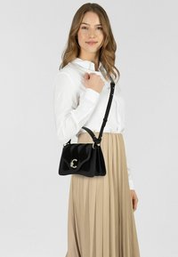 Borsa a tracolla in similpelle nera con finitura lucida, caratterizzata da un design testurizzato, dettagli in oro e tracolla removibile.