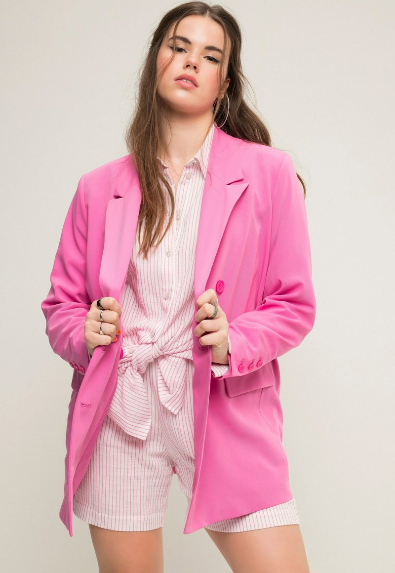 Blazer rosa con hombros estructurados, diseño de un solo botón y detalles de botón. Llevarlo sobre una camisa a rayas y pantalones cortos a juego.
