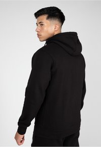 Zwarte hooded sweatshirt met een textuurafwerking, voorzien van een kangoeroezak en geribde manchetten, weergegeven vanuit een linker zijaanzicht.