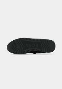 Semelle de chaussure noire avec des motifs géométriques de la bande de roulement et le mot "BOSS" embossé au centre, présenté sur un fond clair uni.