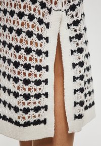 Rochie tricotată cu un model geometric alb-negru, dotată cu o fanta laterală și un material texturat, oferind un aspect ușor și deschis.