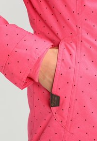 Giacca rosa a pois con una texture morbida, dotata di tasca a mano, polsini elasticizzati e un'etichetta con logo sul lato.
