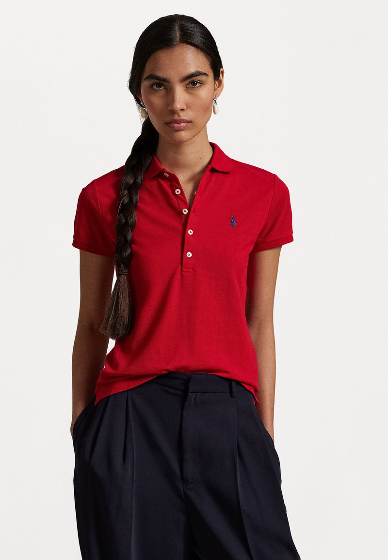 Red polo shirt with a collar and placket, featuring a blue embroidered logo on the chest. Paired with navy high-waisted trousers.