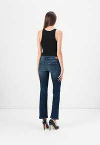 Svart tanktopp kombinert med mørkeblå vide jeans. Jeansene har en baklomme-design og bæres med svarte høye hæler.
