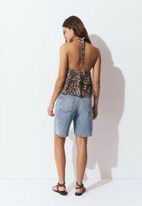 Top halter de estampado de leopardo con un dobladillo con volantes, combinado con pantalones cortos de mezclilla azul claro y sandalias negras con tiras y detalles de tachuelas.