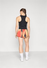 Sort svart uten ermer kombinert med flerfargede shorts med et gradientmønster av oransje, rødt og gult. Hvite sportsokker og sko.