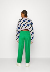Sweater cropped em padrão xadrez multicolorido com preto, roxo, azul e verde, combinado com calças verdes de cintura alta e ténis brancos.