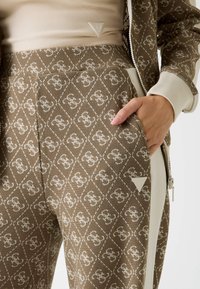 Brązowe spodnie dresowe w wzór diametralny, z boczną kieszenią i kontrastującymi kremowymi akcentami; wykonane z teksturowanej tkaniny.