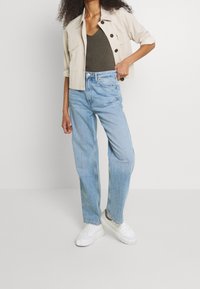 Jasnoniebieskie dżinsy o prostym kroju z wysokim stanem, w połączeniu z jasnobeżową kurtką typu cropped z czarnymi guzikami i podwiniętymi rękawami.