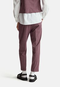 Bordeaux geruite broek met een getailleerde pasvorm, voorzien van rechte benen en omgeslagen zakken, gecombineerd met zwarte sandalen en witte sokken.