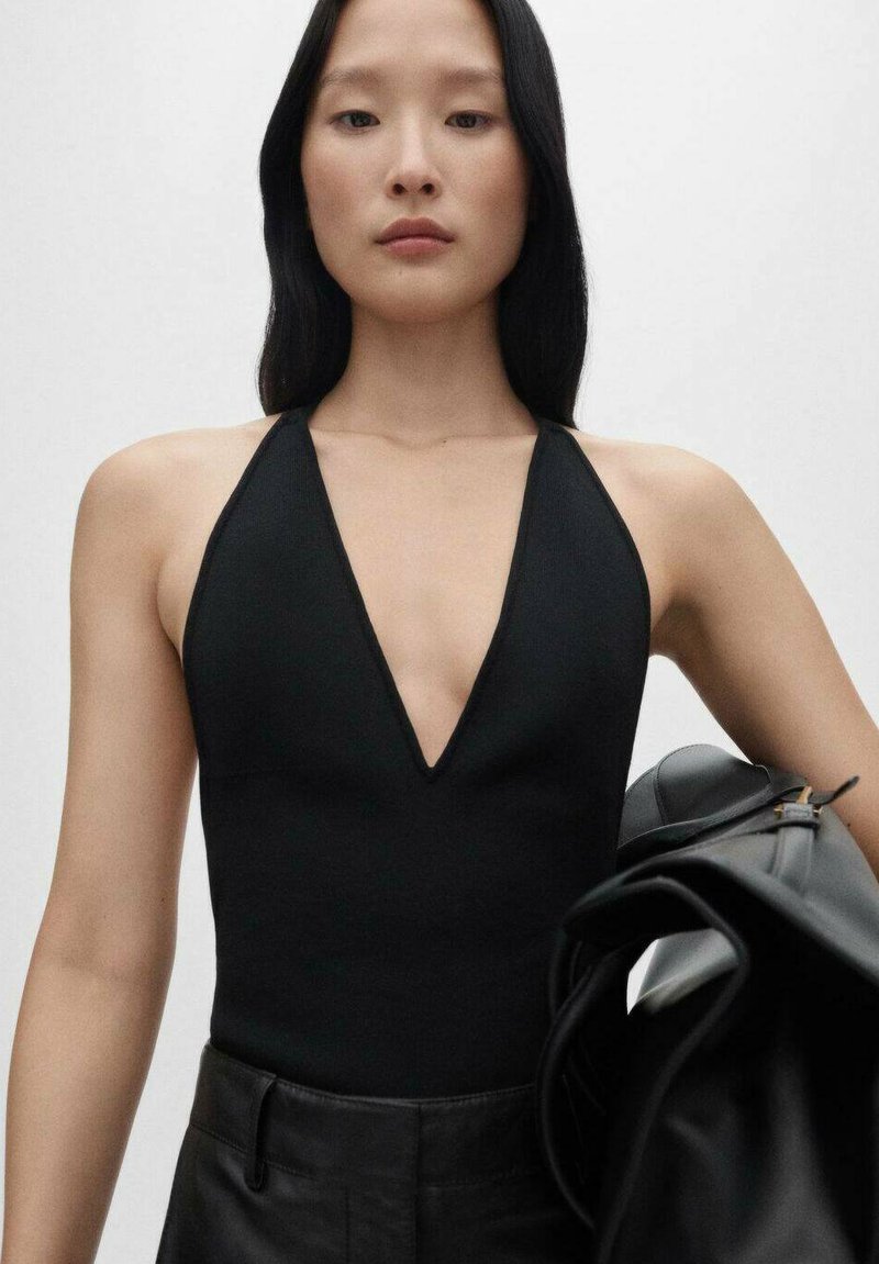 Černý halter bodysuit s hlubokým výstřihem do V, hladká textura, obepínající střih, doplněný o strukturovanou černou koženou tašku.