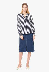 Camicia a righe blu navy e bianca con bottoni e maniche lunghe, abbinata a una gonna a matita in denim scuro con uno spacco anteriore e bordi rifiniti.