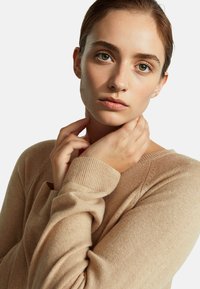 Beżowy sweter dziany z okrągłym dekoltem i ściągaczami. Miękka faktura zawiera widoczne detale przeszycia.