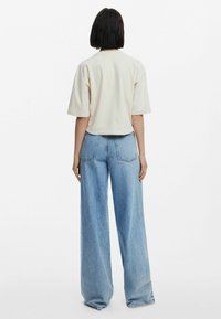 T-shirt crème à manches courtes avec une coupe décontractée, associé à un jean large taille haute bleu clair, présenté de dos.