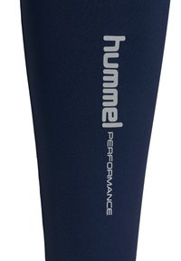 Granatowe legginsy wykonane z elastycznego materiału, z logo "hummel" oraz słowem "PERFORMANCE" w kolorze srebrnym na boku.