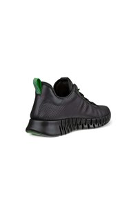 Black athletic shoe with textured upper, contrasting green accents, and a flexible sole featuring pronounced grooves for traction.